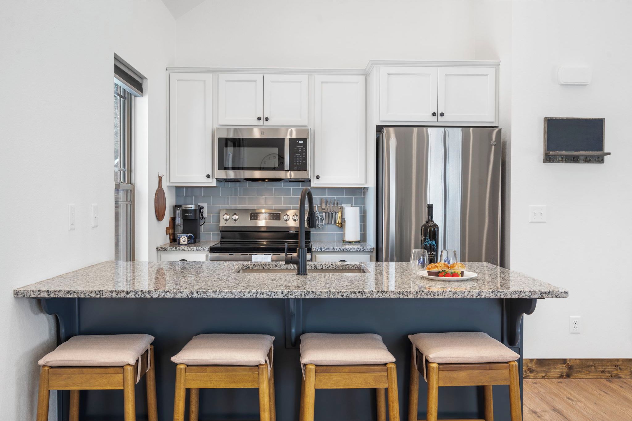 A modern kitchen with white cabinets, stainless steel appliances, a granite countertop, and bar stools.