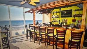 A bar area with a view of the ocean, wooden chairs, and a ceiling fan.