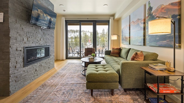 Ein modernes Wohnzimmer mit Kamin, einem grünen Sofa und großen Fenstern mit Blick ins Freie.