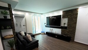 A modern living room with a black leather sofa, a flat-screen TV mounted on a stone wall, and a wooden floor. - TH with private pool in Pampatar, Venezuela (Pampatar)