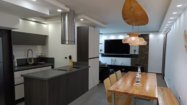A modern kitchen with a central island, a dining area with a wooden table and chairs, and a large TV mounted on the wall. - TH with private pool in Pampatar, Venezuela (Pampatar)