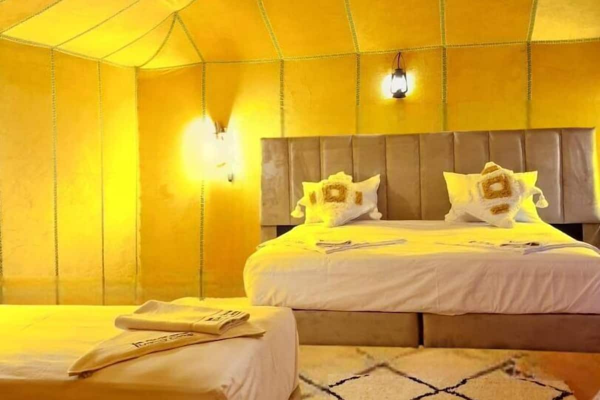 Une pièce aménagée comme une tente, avec deux lits, un luminaire suspendu et des appliques murales.