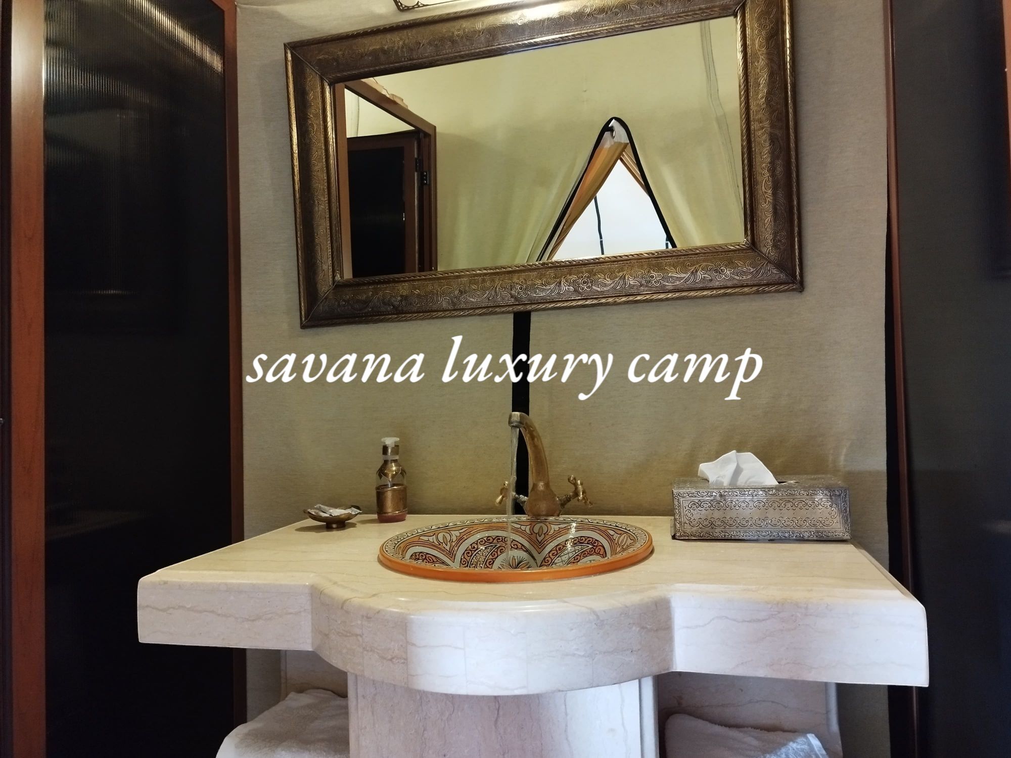 A bathroom with a marble sink, a decorative basin, a tissue box, and a mirror with an ornate frame.