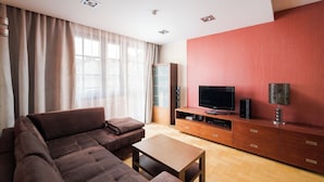Un salon moderne avec un canapé d’angle, un téléviseur posé sur un meuble en bois et une lampe à motifs.