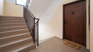 Un escalier avec une rampe, une porte en bois avec une plaque numérotée et une petite fenêtre.