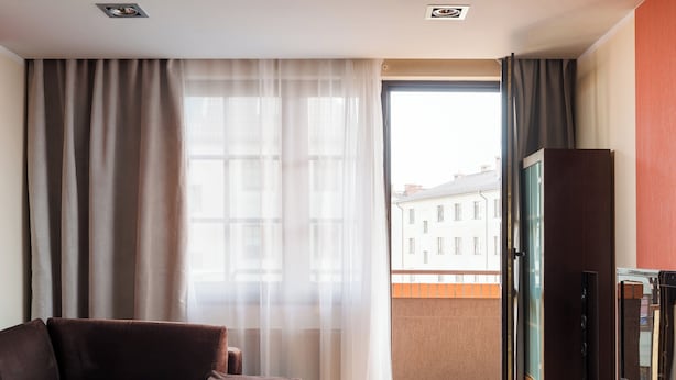 Une chambre d’hôtel moderne équipée d’un canapé, d’un bureau en bois, d’une télévision et d’une grande fenêtre avec des rideaux.