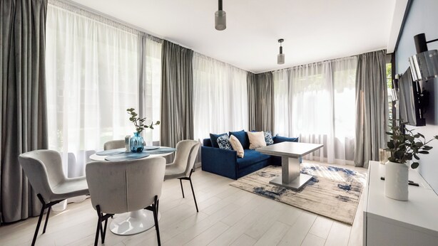 Uma sala de estar moderna com um sofá azul, cadeiras brancas, uma mesa de centro e uma TV em um suporte.