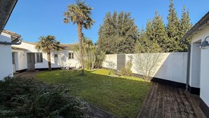 A courtyard with a grassy lawn, a wooden deck, and a white building with a tiled roof.
