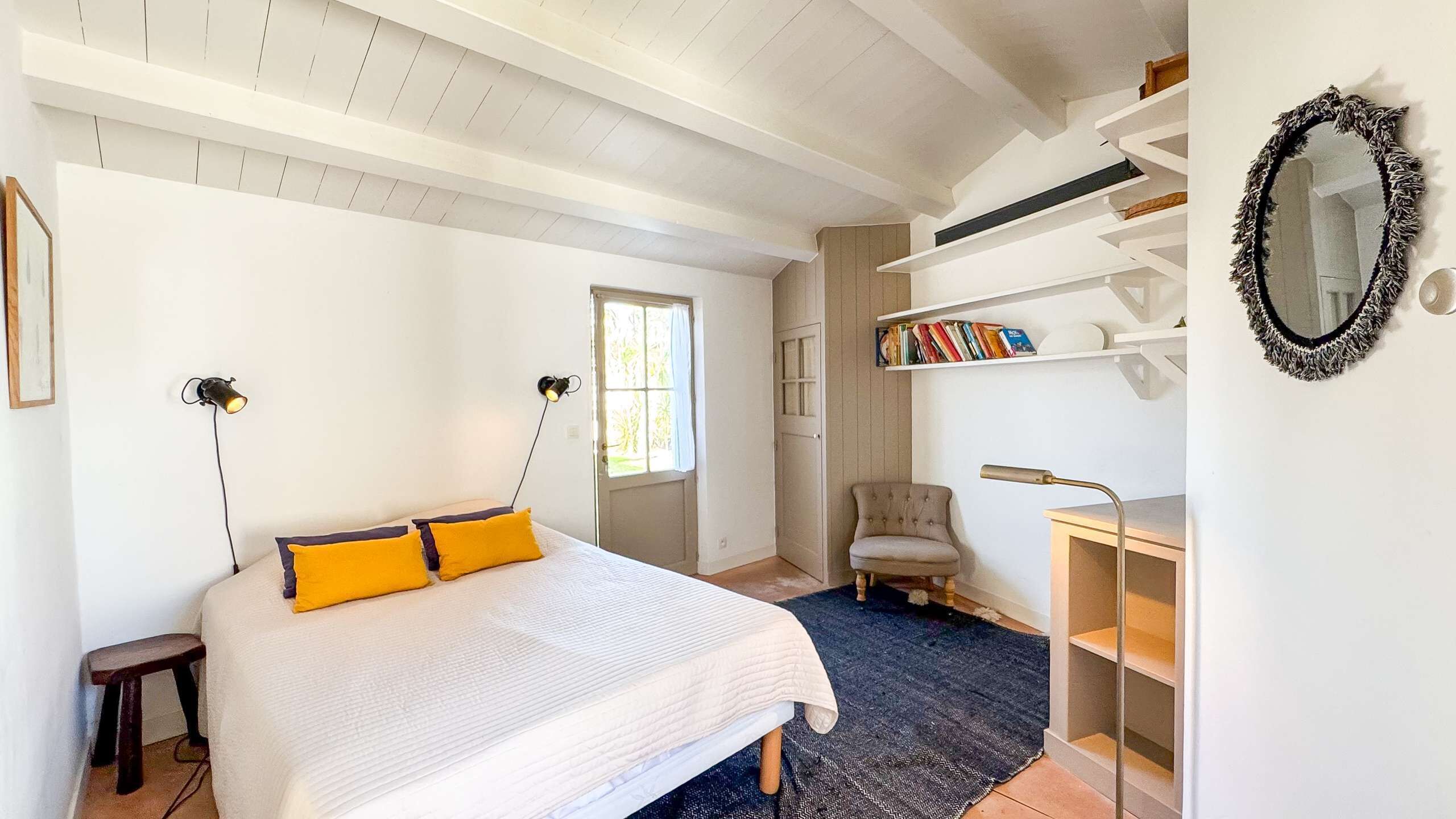 Un dormitorio con cama, lámparas de noche, una silla, escritorio, estanterías con libros y un espejo.