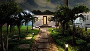 A modern house with a pathway leading to the entrance, surrounded by palm trees and well-maintained grass.