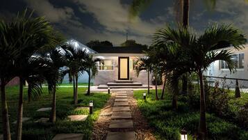 A modern house with a pathway leading to the entrance, surrounded by palm trees and well-maintained grass.