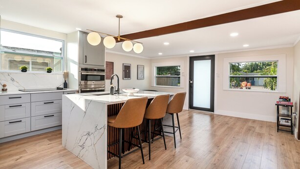 A modern kitchen with a marble island, bar stools, and a pendant light.