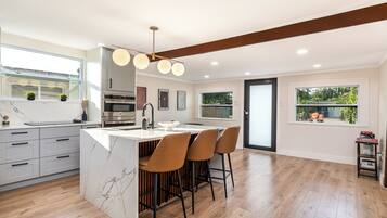 A modern kitchen with a marble island, bar stools, and a pendant light.