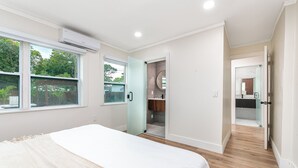A bedroom with a bed, a bathroom with a shower, and a view of greenery outside.