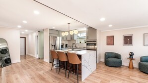 A modern kitchen with a central island, bar stools, and a dining area with a green upholstered chair.