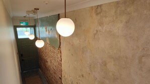 Un couloir aux murs en briques apparentes, avec une porte verte et des luminaires sphériques suspendus au plafond.