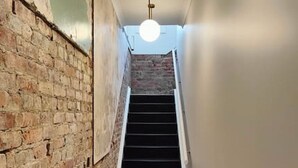 Un couloir étroit, avec un mur de briques d’un côté et un escalier menant à l’étage supérieur.