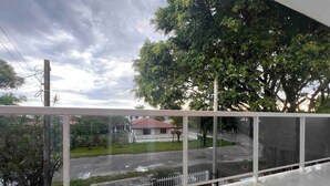 Un balcone con vista su una strada, una casa e degli alberi.