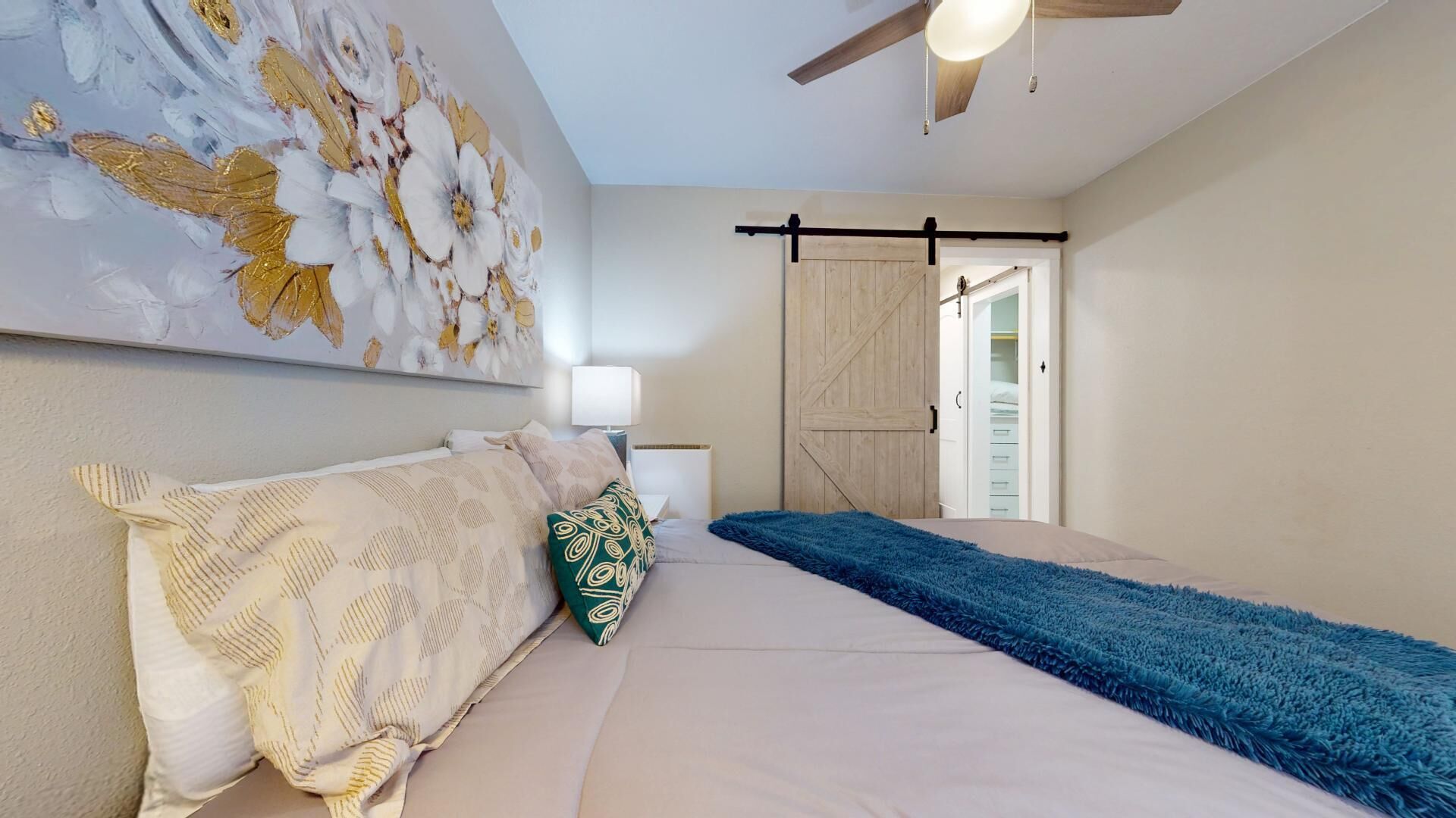 Une chambre à coucher comprenant un lit, une table de chevet, une lampe, un placard avec porte coulissante et un ventilateur de plafond.