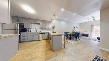 A modern kitchen with grey cabinets, a central island, and a dining area with blue chairs.