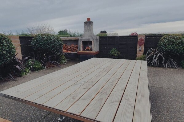 A wooden deck with a built-in barbecue grill and a stone chimney, surrounded by greenery. - Gorgeous in the Glen (Mill Road)
