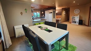 Un comedor con una mesa blanca y sillas negras, una cocina al fondo y un reloj en la pared.
