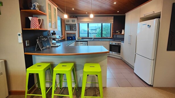Una cocina moderna con una isla central, taburetes de color verde brillante y un amplio ventanal que proporciona luz natural.