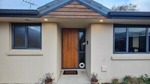 Una casa moderna con puerta de madera, dos plantas en macetas y un pequeño porche.