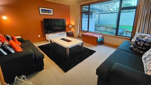 Una sala de estar con sofá, una mesa de centro, televisor y un ventanal grande.