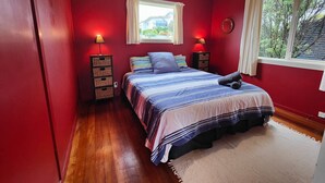 A bedroom with a bed, two bedside tables, a window with curtains, and a view of greenery outside. - Riverton Beachhouse View (Riverton / Aparima)