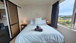 A hotel room with a bed, a desk, a chair, a window with a view, and a lamp on the nightstand.