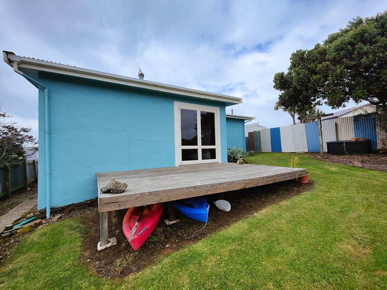 A blue house with a wooden deck and a red kayak underneath.