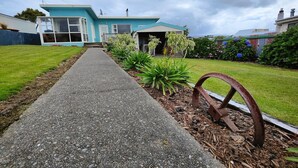A pathway leading to a house with a satellite dish, a garage, and a garden with plants and a metal wheel.