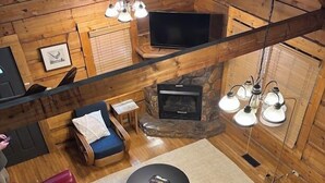 A cozy cabin interior with a stone fireplace, red leather sofas, a flat-screen TV, and wooden walls. - Dockside Cabin | RRG | Hot Tub | Kayaks | Fire Pit (Campton)