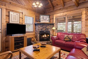Un intérieur de chalet chaleureux avec une cheminée en pierre, un canapé en cuir, une table basse en bois et un téléviseur à écran plat.