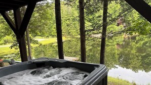 A hot tub with a wooden deck and a view of a lake and trees. - Dockside Cabin | RRG | Hot Tub | Kayaks | Fire Pit (Campton)