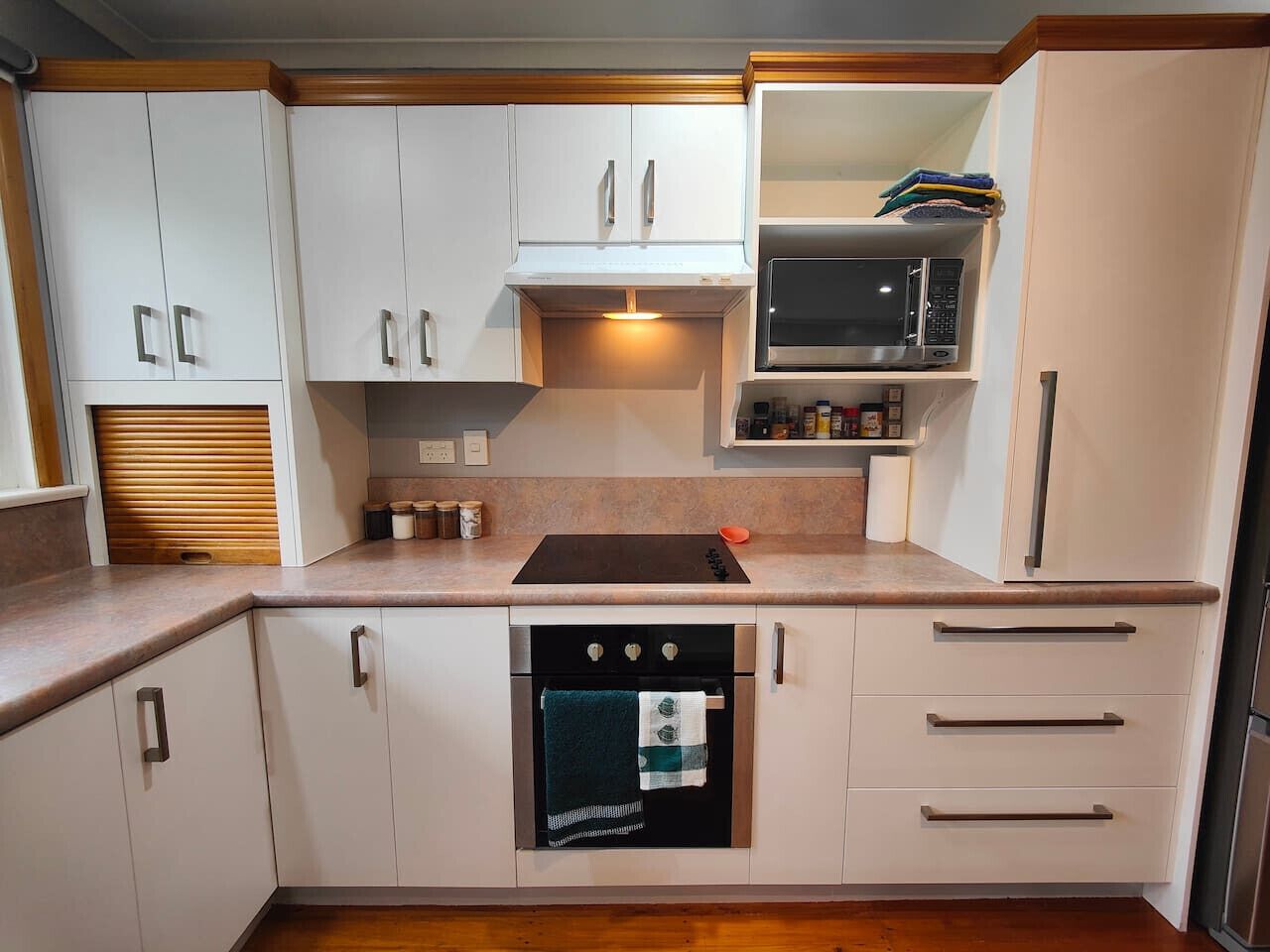 A compact kitchen with white cabinets, a built-in oven, a microwave, and a countertop with a kettle.