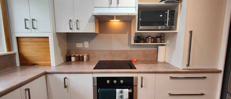 A compact kitchen with white cabinets, a built-in oven, a microwave, and a countertop with a kettle.