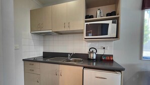 Una cocina compacta con armarios de madera clara, un microondas integrado, una tetera y un lavavajillas.
