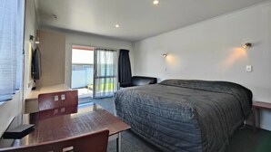 Habitación de hotel con cama, escritorio y silla. Tiene ventana con cortinas, puerta y vistas al exterior.