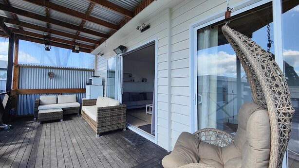 Ein überdachter Außenbereich mit Holzdeck, Korbmöbeln und einem Hängesessel.
