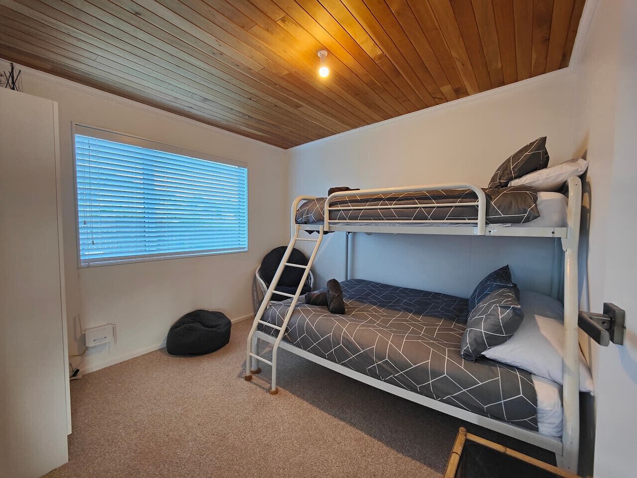 Een slaapkamer met stapelbed, raam en een slaapzak.