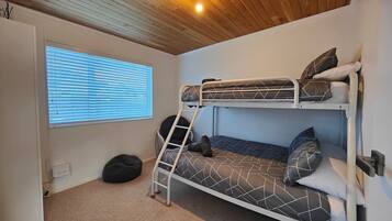 Een slaapkamer met stapelbed, raam en een slaapzak.