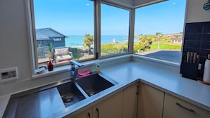 A modern kitchen with a large window offering a view of the sea and a house. - Riverton Helm`s Deep (Riverton / Aparima)