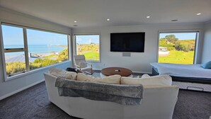 A modern living room with a large window, a flat-screen TV, a sofa, a chair, and a small table. - Riverton Helm`s Deep (Riverton / Aparima)