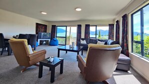 Un salon spacieux comprenant un canapé, des fauteuils, une table basse et un téléviseur. De grandes fenêtres offrent une vue sur les montagnes.