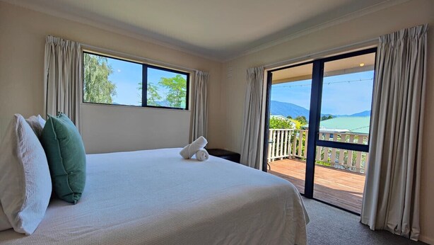 Une chambre d’hôtel avec un grand lit, deux oreillers, une vue sur un balcon avec une balustrade et une fenêtre avec des rideaux.