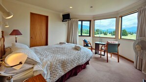 A hotel room with a large bed, a desk, a chair, a TV, and a view of the outdoors. - Te Anau Dusky Delight (Te Anau)