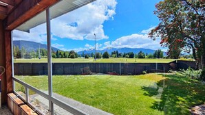 A view from a room with large windows overlooking a grassy yard with a fence, trees, and mountains in the background. - Te Anau Retro Retreat (Te Anau)