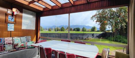 Un salón de conferencias con una gran mesa y sillas, un banco de madera con cojines, y vistas a un área verde con árboles y montañas al fondo.